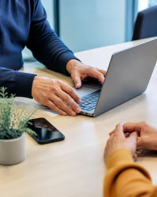 Hands setting up a new laptop at a desk beside a phone and a plant